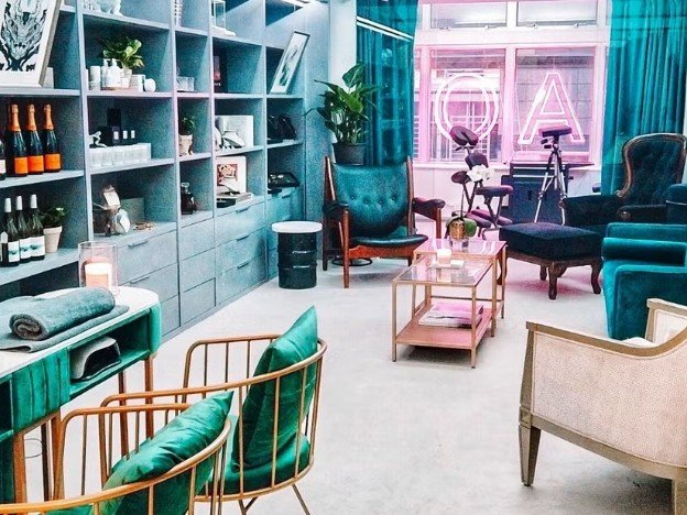 The Kaos studio: teal velvet chairs, gold-framed furniture and a pink neon sign by the window.